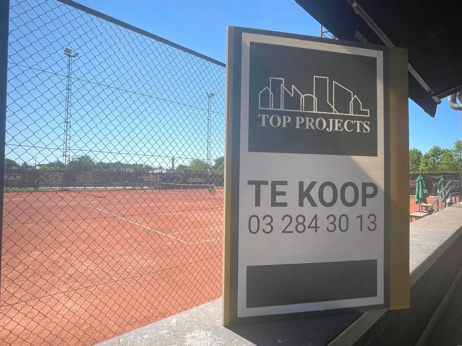 Te koop bord van Top Projects langs het tennisterrein